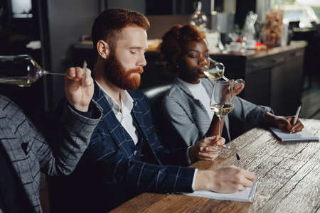 Sommeliers female and male tasting white wine and making notes at degustation card notepadの写真素材