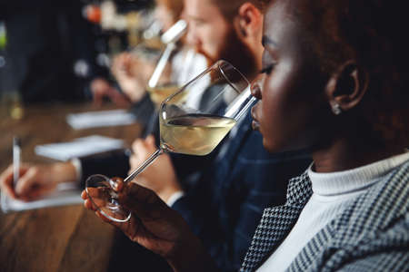 African woman sommelier bartender smelling white wine and making degustation cardの写真素材