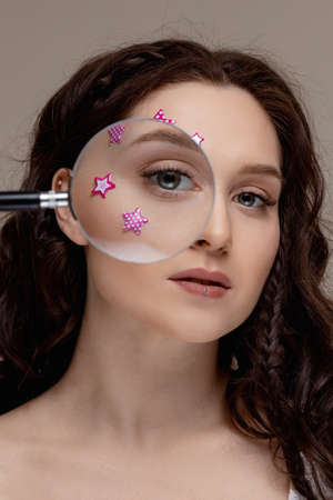 Concept creative fashion photo girl eyelash extensions in salon. Portrait brunette woman holding magnifying loupe over eyeの写真素材