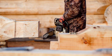 Industrial work carpenter sawing with chainsaw log, construction frame building site of house made of woodの写真素材