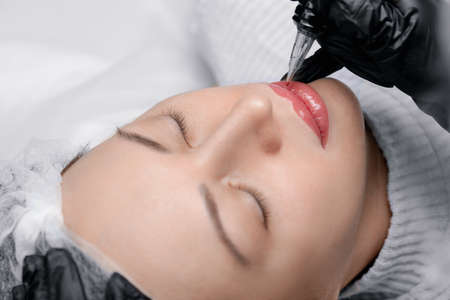 Process applying permanent makeup tattoo of red on lips woman in beautician salonの写真素材