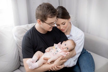 Young parents Father holds newborn baby girl in arms, mother hugs family, sun light top viewの写真素材