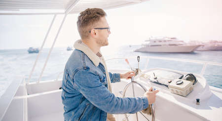 Concept rental or training driver man captain of white luxury yacht holding helm wheel, summer tripの写真素材