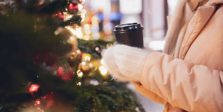 Christmas market, closeup cup hot coffee on hand woman, garland bokeh light evening. Banner winter vacations in Red square Moscow, Russiaの写真素材