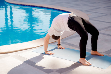 Meditation yoga man asana bridge pose background pool, palm trees and sunlightの写真素材