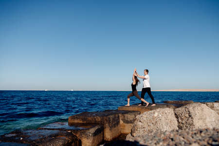 Personal trainer man correct woman client while doing stretching or yoga outdoors background sea. Concept asana instructor supportの写真素材