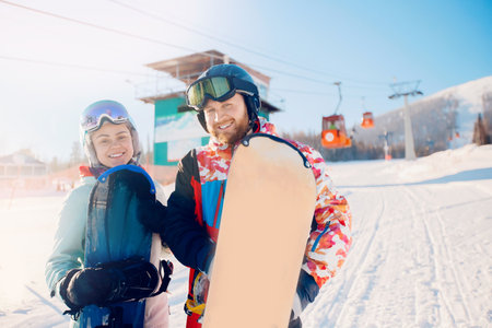 Happy young couple man and woman snowboarders on background of ski resort sun winter dayの写真素材