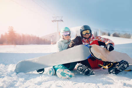Happy young lover couple man and woman snowboarders on background of ski resort, sun lightの写真素材