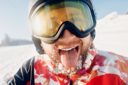 Portrait smile young bearded man with fresh snow holding snowboard background of ski resort lift, sun lightの写真素材