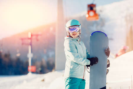 Portrait young woman snowboarder stands with snowboard sunlight, winter ski lift resortの写真素材