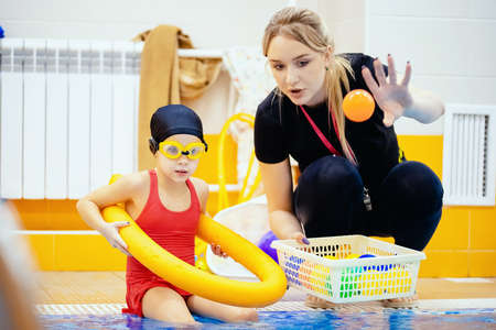 Child girl is practicing swimming in pink bathing suit in pool, coach will conduct training swimの写真素材