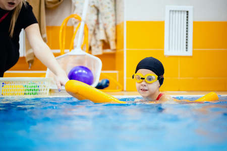 Child girl is practicing swimming in pink bathing suit in pool, coach will conduct training swimの写真素材