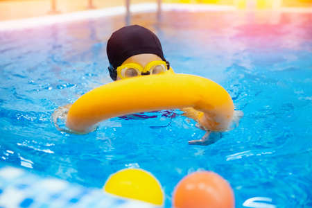 Little kid girl with glasses learning to swim with pool yellow noodle. Concept training swimming childの写真素材