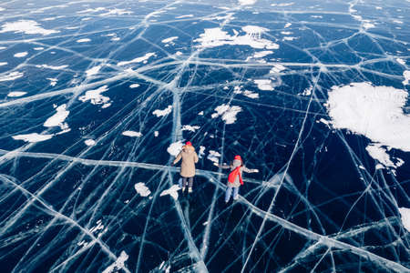 Winter lake Baikal Russia, two tourist women friends in red cap are skating on ice frozen, sunny day. Concept freedom lifeの写真素材