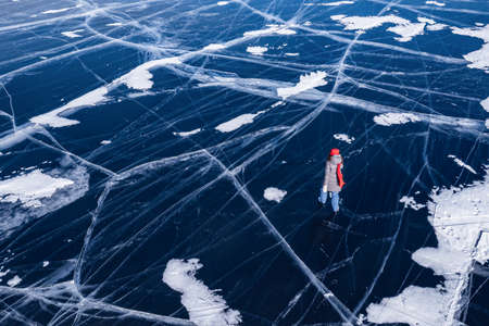 Freedom Woman tourist on ice skates and with long red scarf on frozen lake Baikal. Aerial top viewの写真素材