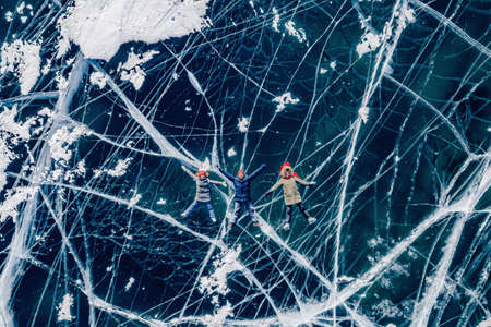 Group tourists man and two women on ice of frozen Lake Baikal in winter. Aerial top viewの写真素材