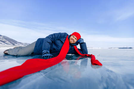 Travel winter Lake Baikal, smile man tourist in red cap lie on iceの写真素材