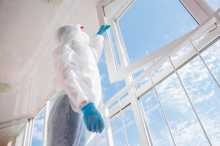 Woman wearing protective biohazard due mers global pandemic warning. Cleaning service disinfects, pest control glass windows from virusの写真素材
