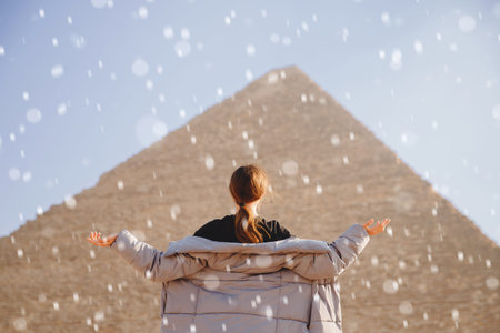 Winter snow on background of Pyramids of Cheops Egypt tourist girl in warm jacket. Concept anomalous...