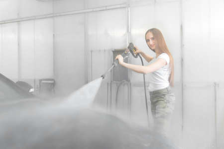 Car washing service. Worker woman cleaning auto using high pressure waterの写真素材