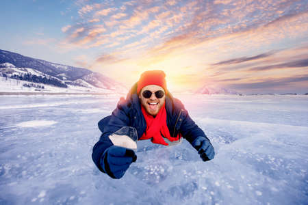 Portrait happy male tourist in red hat with shard of transparent ice in winter on Lake Baikal sunsetの写真素材