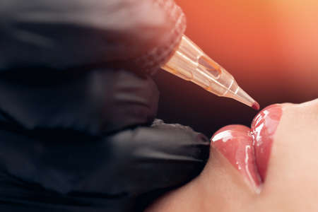 Macro photo of process of applying permanent makeup tattoo of red on lips womanの写真素材