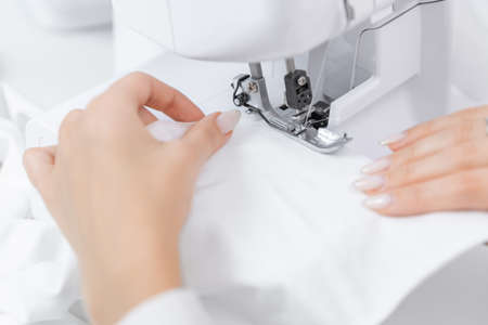 Fashion dressmaker young woman sews clothes on sewing machine in factory, white backgroundの写真素材