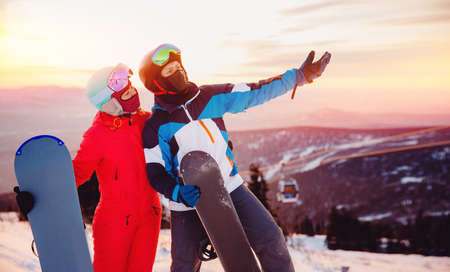 Concept friends travel love winter sport. Happy couple man and woman snowboarders background sunset ski resortの写真素材
