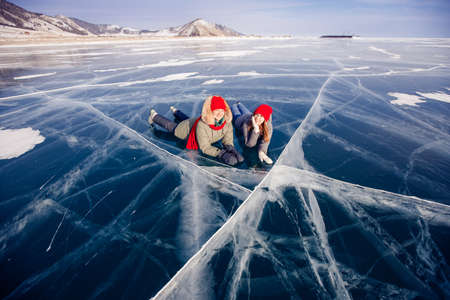 Two young women friends in red cap are skating on ice frozen of Baikal lake, winter sunny dayの写真素材
