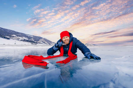 Happy man tourist in red cap bites transparent ice in winter on Lake Baikalの写真素材