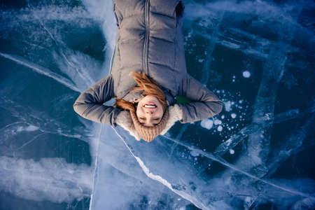 Travel winter Lake Baikal, happy young woman tourist lie on blue iceの写真素材