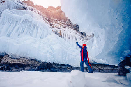 Man traveler in red hat and scarf against background of grotto and pure ice winter Lake Baikalの写真素材