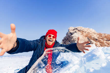 Adventure travel in winter, tourist man with red scarf makes selfie background ice grotto and cave, frozen icicles of Lake Baikalの写真素材