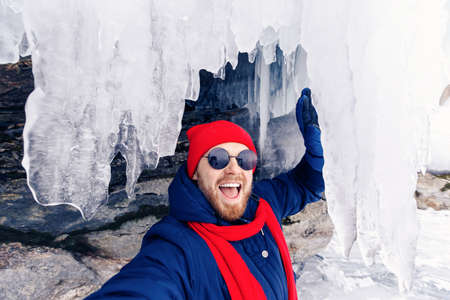 Adventure travel winter tourist man with red scarf background ice grotto and cave, frozen icicles of Lake Baikalの写真素材