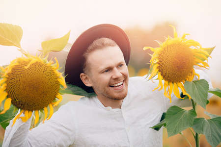 Smile caucasian farmer worker man in hat in sunflowers field sunlight. Concept lifestyle summer happyの写真素材