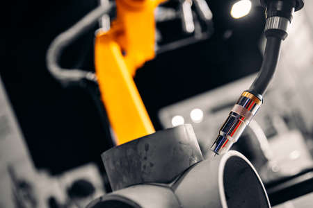 Closeup yellow arm robot welding metal pipe part in industry factoryの写真素材