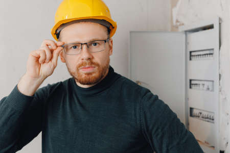 Portrait foreman man in yellow helmet inspecting electrical panel and work of electrician in apartmentの写真素材