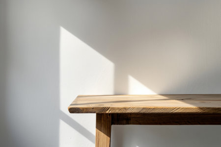 Minimalist wooden table against a white wall with sunlight casting a shadowの素材