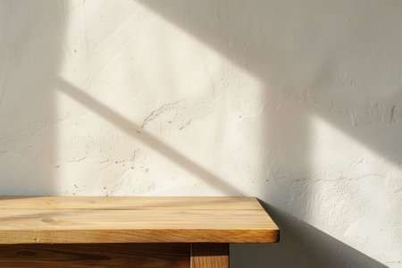Minimalist wooden table against a white wall with sunlight casting a shadowの素材