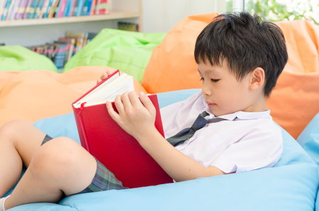 Asian schoolboy reading book in school library