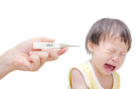 Woman\'s hand holding digital thermometer and crying baby sitting in backgroundの写真素材