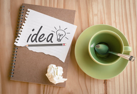 Notebook with text inside Idea and light bulb on table with empty coffee cupの写真素材