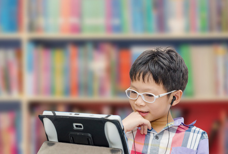 Little Asian boy using tablet computer and earphone in libraryの写真素材