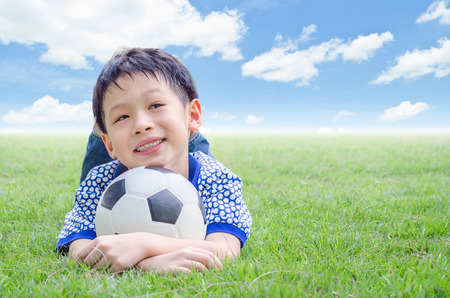 Little Asian boy smiles with his football on fieldの写真素材