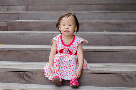 Little Asian girl sitting and smiling outdoorの写真素材