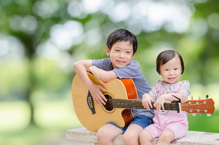 Asian boy and his younger sister play guitar and sing in gardenの写真素材