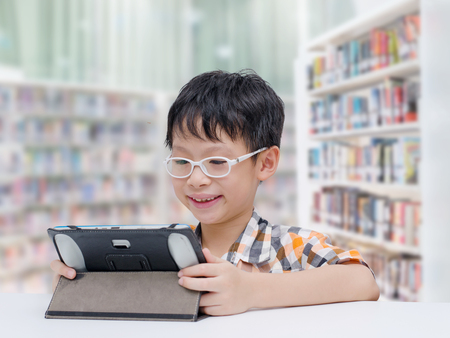 Asian boy student searching information by tablet computer in school libraryの写真素材