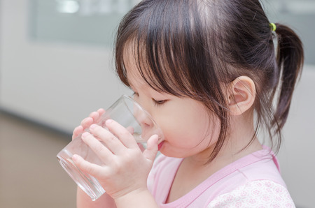 Little Asian girl drinking water from glassの写真素材