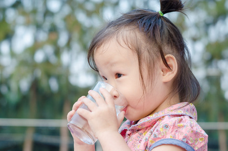 Little Asian girl drinking water from glassの写真素材