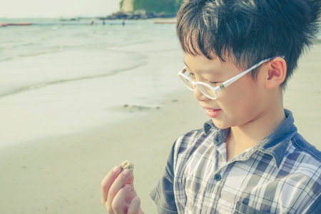 Young boy looking at shell on the beach with vintage filter